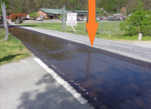 The arrow in this image points out the strip of tack that is “oversprayed” on the chip. Due to the 18-foot width of this section of roadway, the chip spreader had to make two passes. That means the tack wagon also made two passes to ensure good tack gave the aggregate good adhesion.