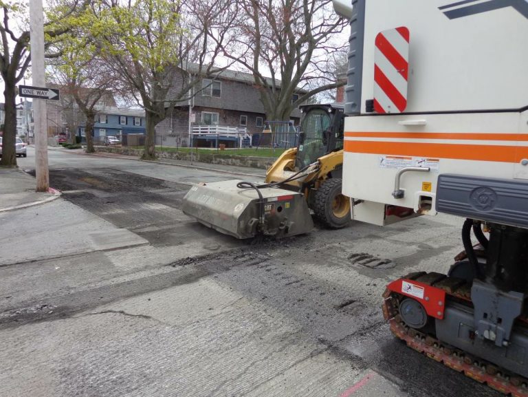 The broom on the city street may require a system to capture material and dust. This skid steer will routinely empty the bucket of millings into a waiting truck body.